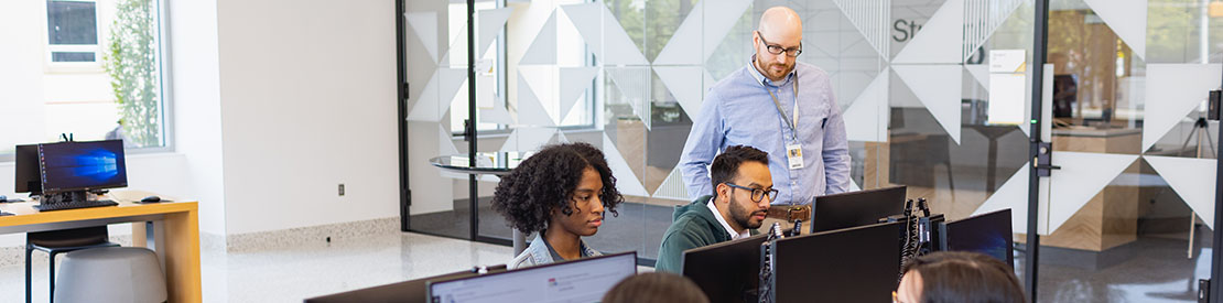 diverse students looking at their computer screens with instructor standing next to them