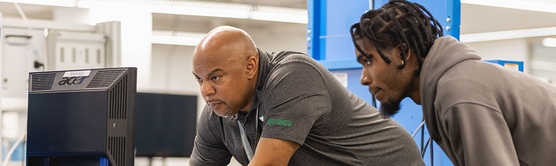 instructor and student looking at computer beside equipment