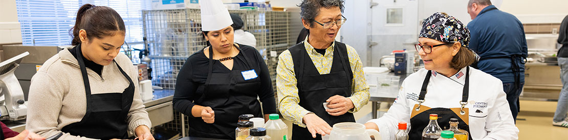 diverse group of people in aprons in kitchen cooking class