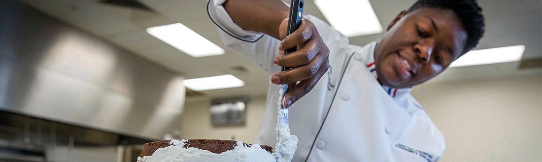 baking hospitality student icing a cake 