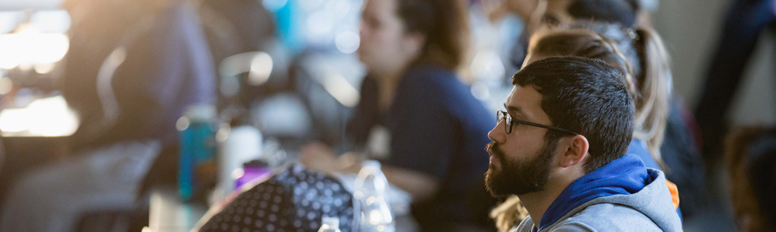 diverse students sitting in classroom looking at the front of the class.